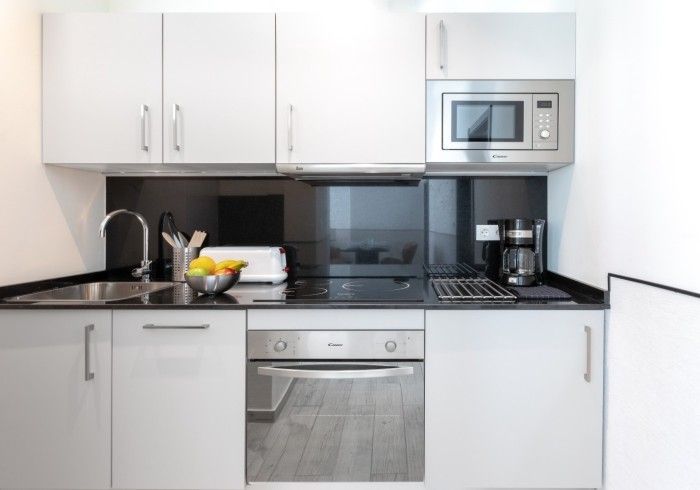 Cocina moderna con gabinetes blancos, encimeras negras, horno empotrado, microondas y cafetera.
