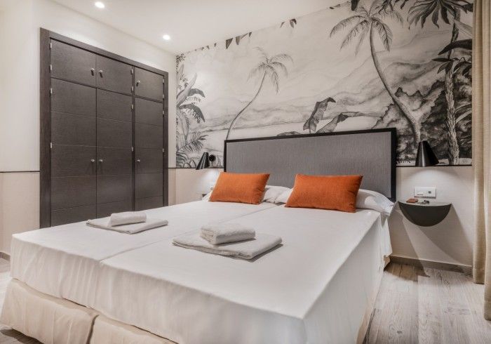 Dormitorio moderno con una cama grande, almohadas naranjas y un mural en la pared detrás.