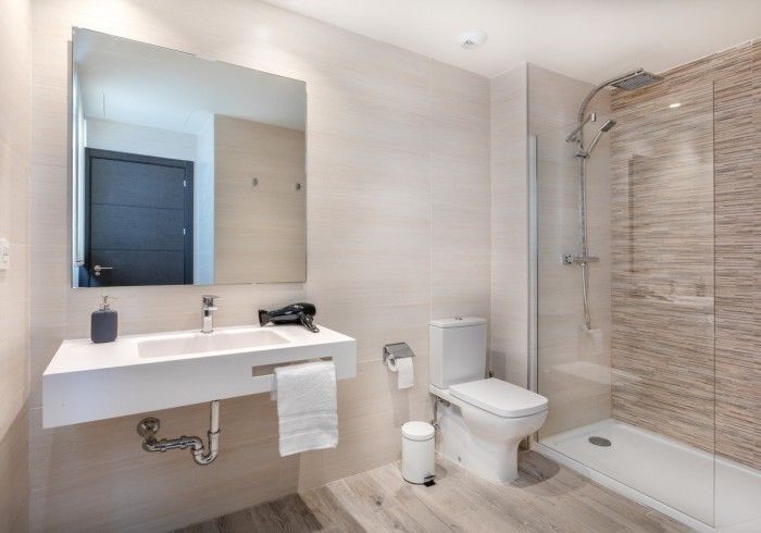 Baño moderno con lavabo mural, inodoro, espejo y cabina de ducha de cristal.