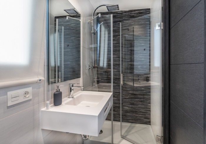 Baño moderno con ducha de cristal, espejo de pared y lavabo suspendido en tonos grises.