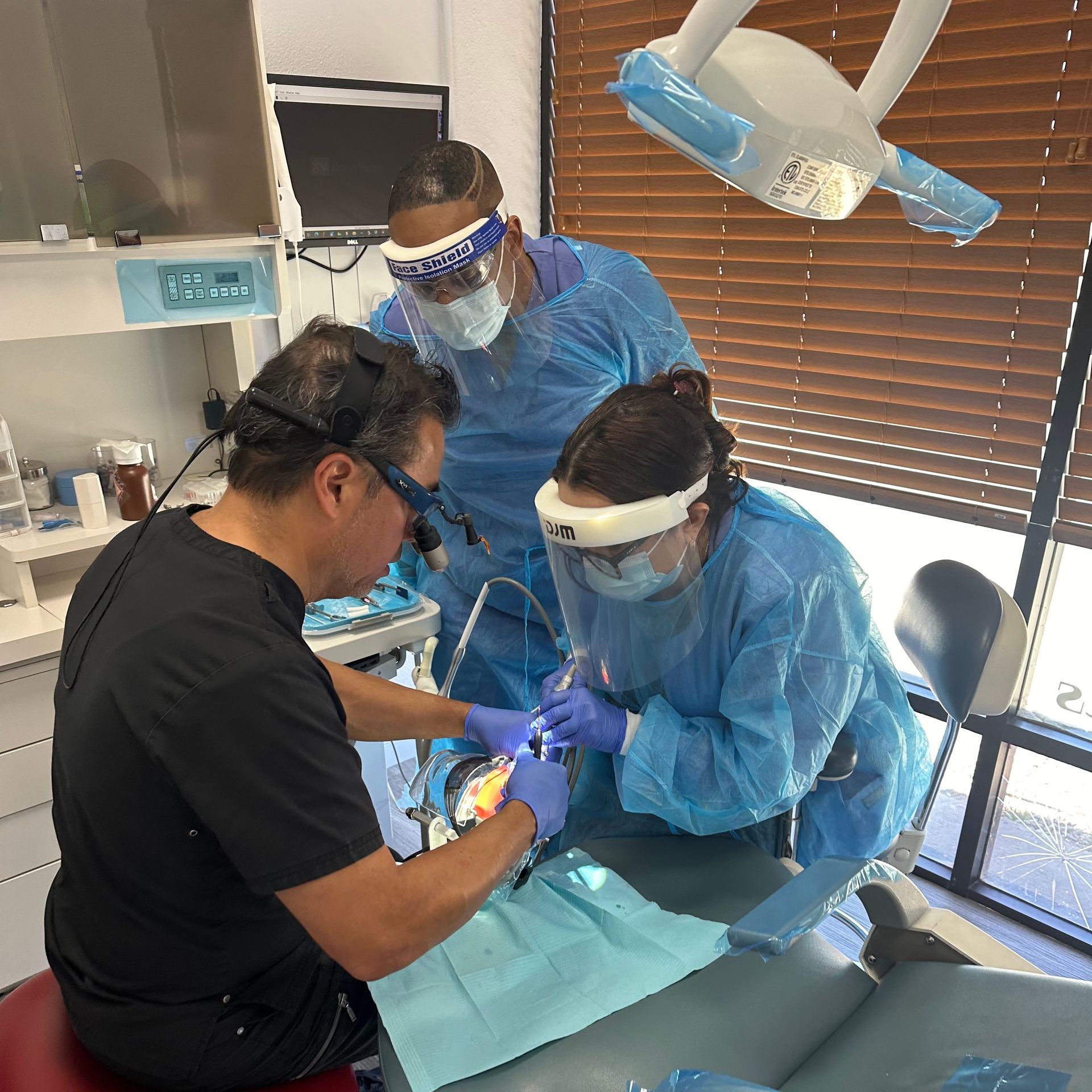 Dentist and assistants in protective gear performing dental procedure. In a dental office.