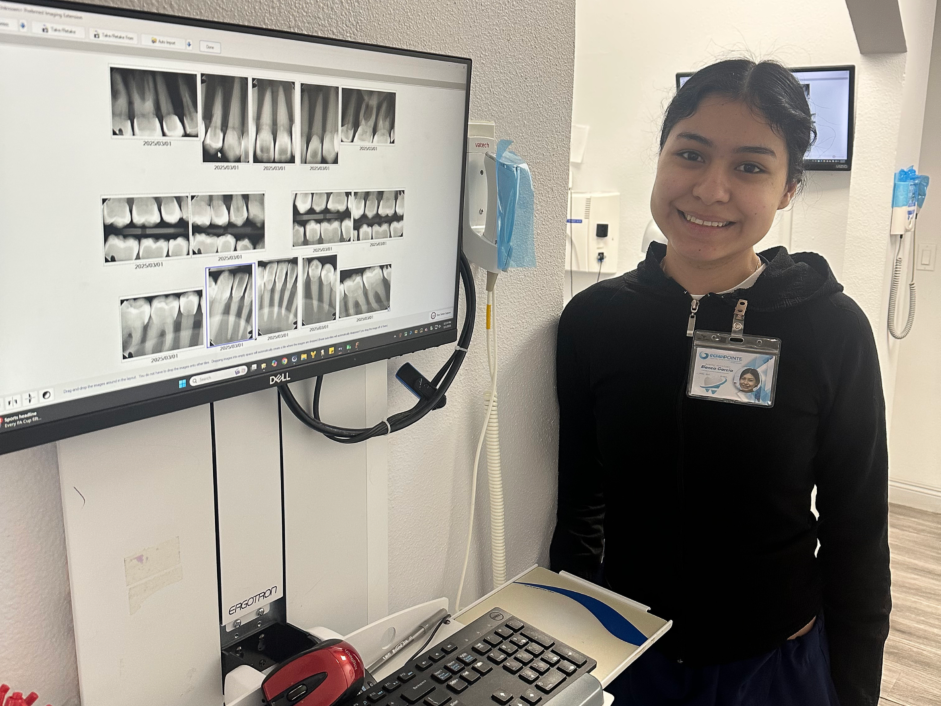 Woman in black sweater smiles beside dental x-ray screen. Dental office setting.
