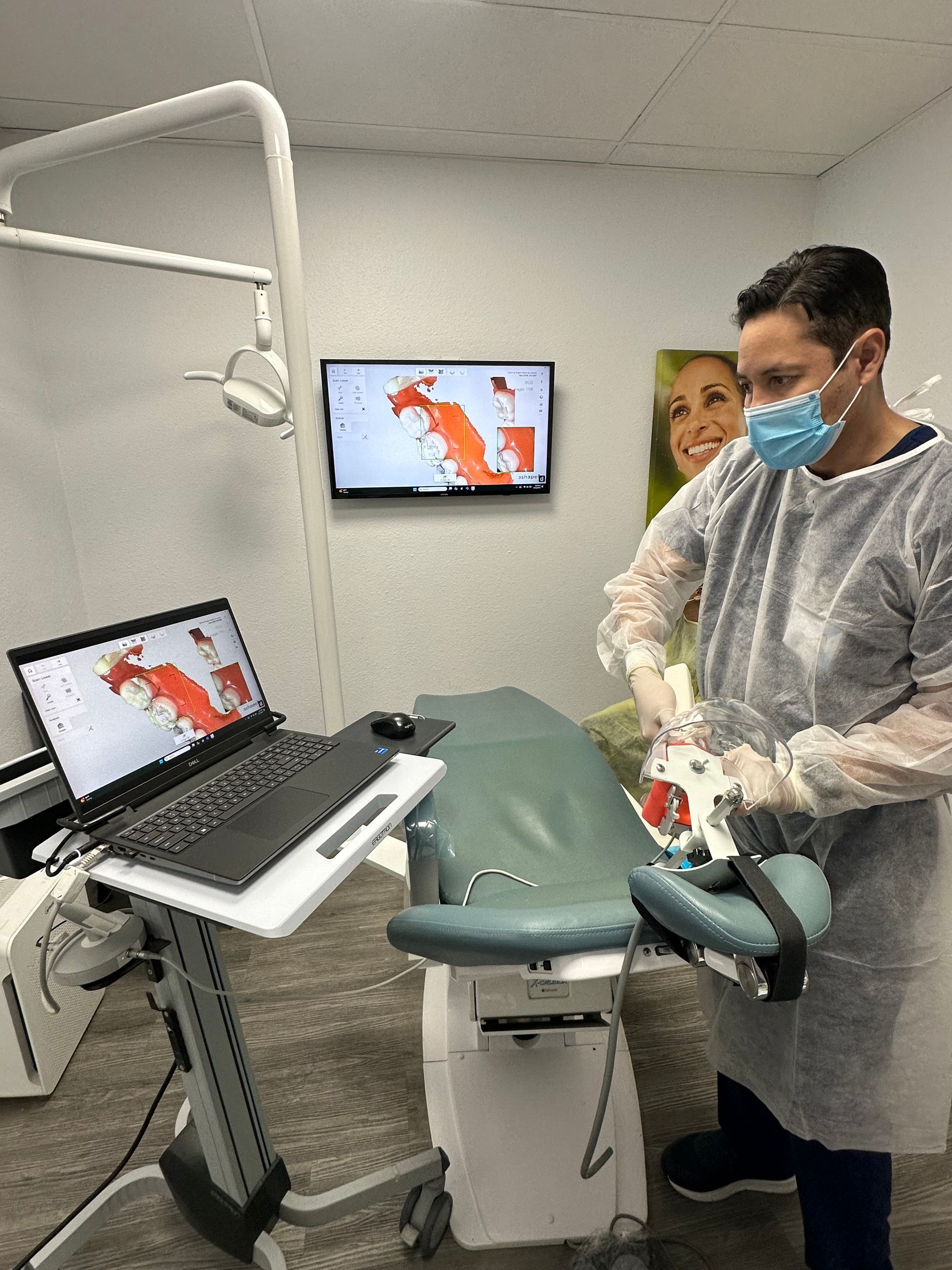 Dentist in mask and gloves examining a patient's mouth, with monitors displaying oral scans.
