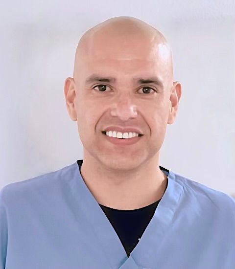 Ray Carrillo, smiling, wearing a blue scrub top and a black shirt underneath.