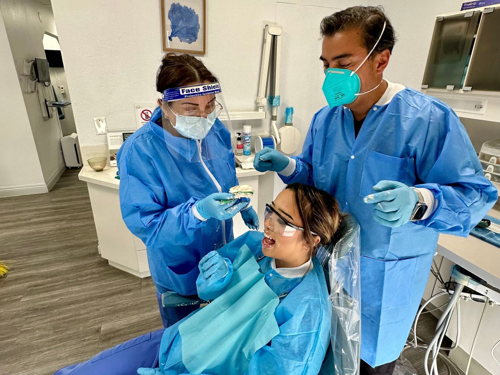 Dentists in protective gear examining a patient in a dental office.