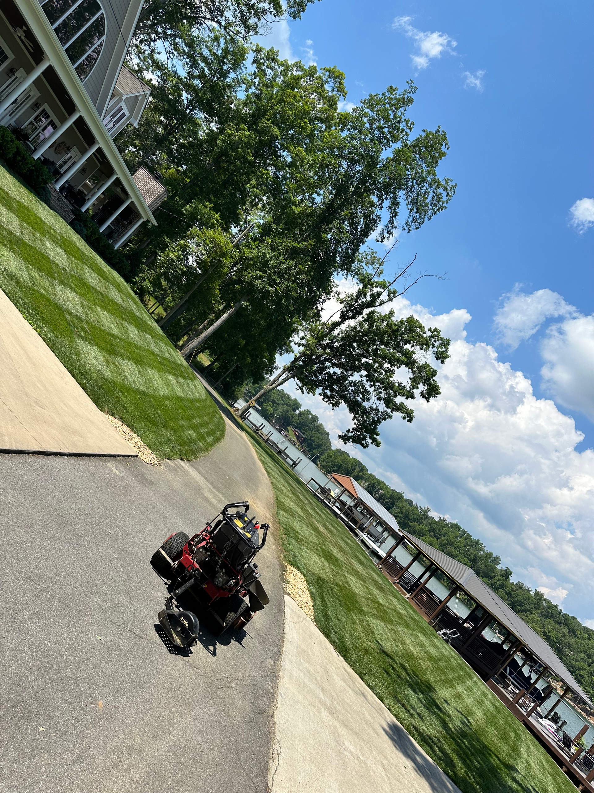 A red all-terrain wheelchair on a paved path near a grassy lawn and a lake under a blue sky.