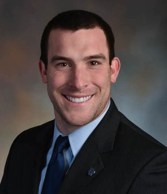 A man in a suit and tie is standing with his arms crossed.
