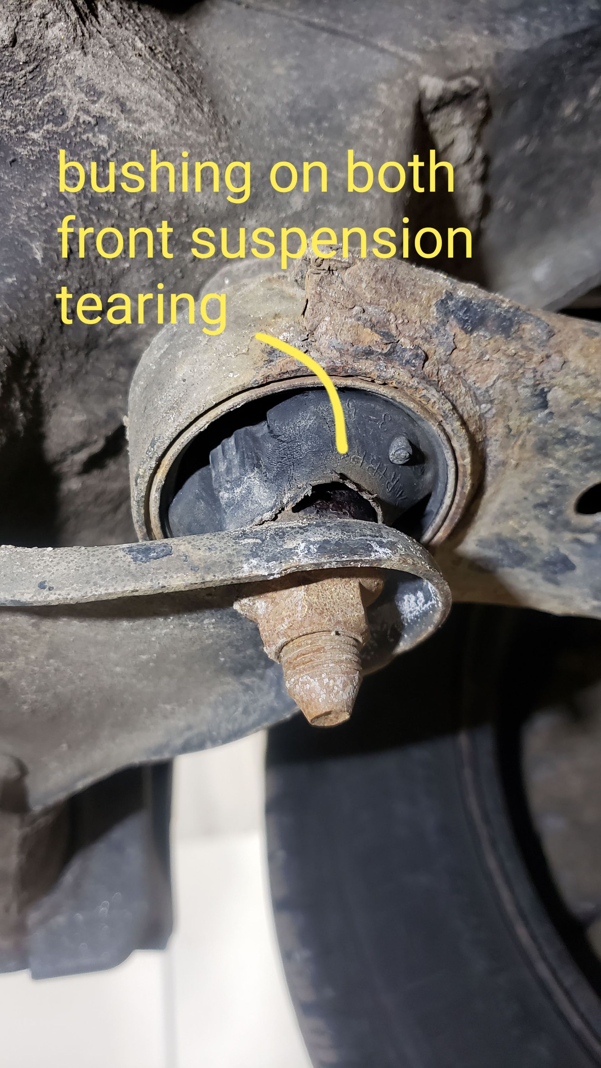 Torn suspension bushing on a vehicle's front suspension arm, causing a tear in the rubber.