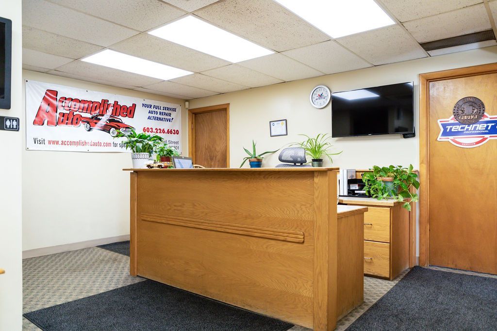 Reception area with a wooden counter, door, TV, and clock. | Accomplished Auto