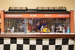 Miniature auto repair shop model with glass walls and figures.