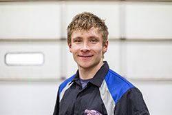 Smiling person wearing a blue and black work shirt, standing in front of a white garage door.