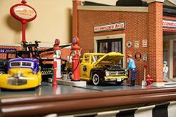 Miniature auto shop scene with a tow truck, a mechanic working on a yellow truck, and gas pumps.