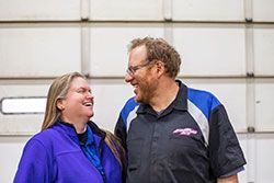 Two people, a woman and a man, smiling and looking at each other in front of a white garage door.