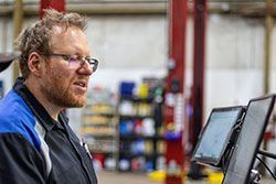 Mechanic in blue and black work shirt looks at a screen in a garage.