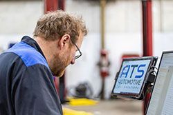 Mechanic in blue uniform uses a tablet at ATS Automotive.