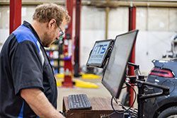 Mechanic in a blue and black uniform looking at a computer screen in an auto repair shop.