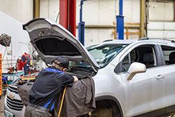 Mechanic working on a silver SUV in a garage with the hood open.
