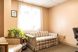 Waiting room with sofa, chair, window, potted plant, and framed art.