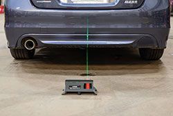 Rear of a blue car with a laser alignment tool on the ground. A green laser line projects up to the car.