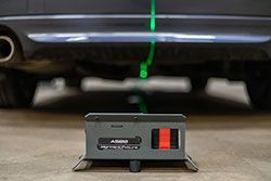 A black car's undercarriage with a laser alignment tool projecting a green line.