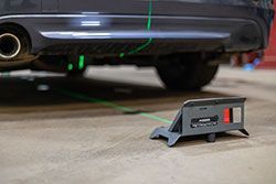 Car's undercarriage with a laser alignment tool on the ground, projecting green lines.