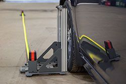 Measuring tool positioned near a car wheel, likely for alignment or inspection. Yellow tape measure extended.