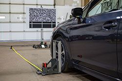 Car wheel aligned in a shop with black and gray equipment, and a pattern screen in background.