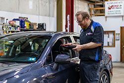 Mechanic uses diagnostic tool on a blue car in a garage.
