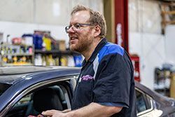 Man in mechanic uniform leaning on a car in a garage.