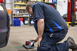Mechanic kneeling, using a laser level to align a vehicle's tire in a garage.