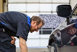 Mechanic in blue uniform inspects car wheel in a garage.