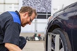 Mechanic checks car tire alignment with equipment in a shop.