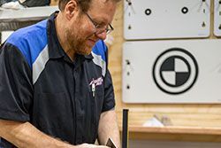 Mechanic working on equipment in a shop, wearing glasses and a blue and black uniform.