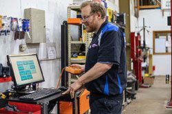 Mechanic in a garage using a computer and diagnostic tool to assess a car.