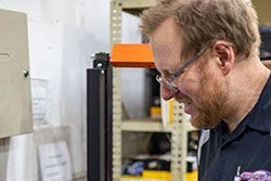 Man with glasses looking down at a machine, in a workshop setting.