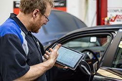 Mechanic using a tablet diagnostic tool on a car in a garage.