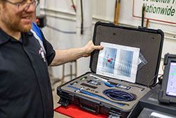 Mechanic holding a diagnostic tool kit, looking at a diagram, next to a machine.