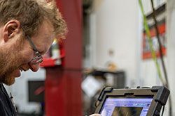 Mechanic using a tablet to diagnose a vehicle, looking intently.