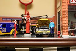Miniature garage scene with a yellow car, mechanic, and gas pump.