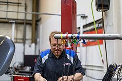 Mechanic working on equipment in a shop, using colored wires and tools.