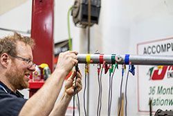 Mechanic attaching wires to a metal bar with colored tape. Shop interior; focus on his hands.