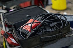 Diagnostic tool in black case with coiled cables. Red and black tool visible.