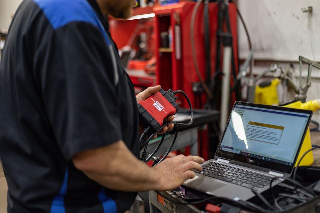 Mechanic using diagnostic tool and laptop in a repair shop. | Accomplished Auto