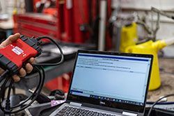 A person using a diagnostic tool connected to a laptop to analyze car data in a garage.