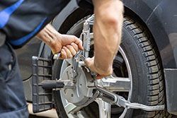 Mechanic using alignment equipment on a car tire in a garage.