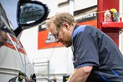 Mechanic working on a car, inspecting its underside in a garage.