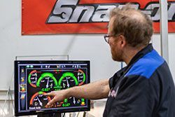 Mechanic pointing at a computer screen displaying car alignment data in a shop. A 