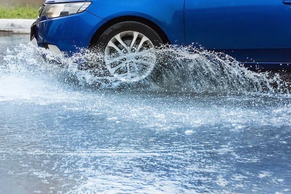 Blue car driving through a puddle, splashing water.