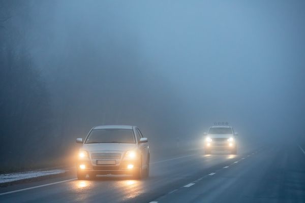 Cars driving on a foggy road with headlights on, visibility limited.