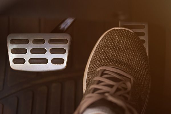 Foot pressing a car pedal; metal pedals on black floor.